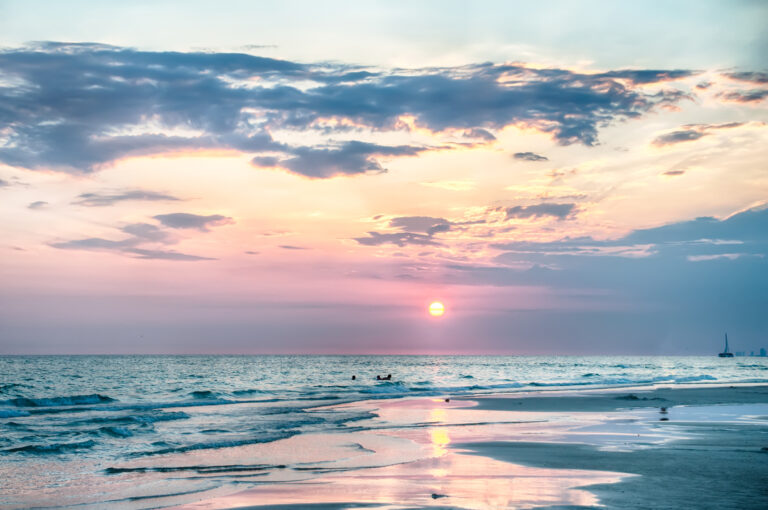 A sunset over a calm ocean with gentle waves, a sandy beach in the foreground, and scattered clouds makes it the perfect scene for Airbnb stays in Florida.