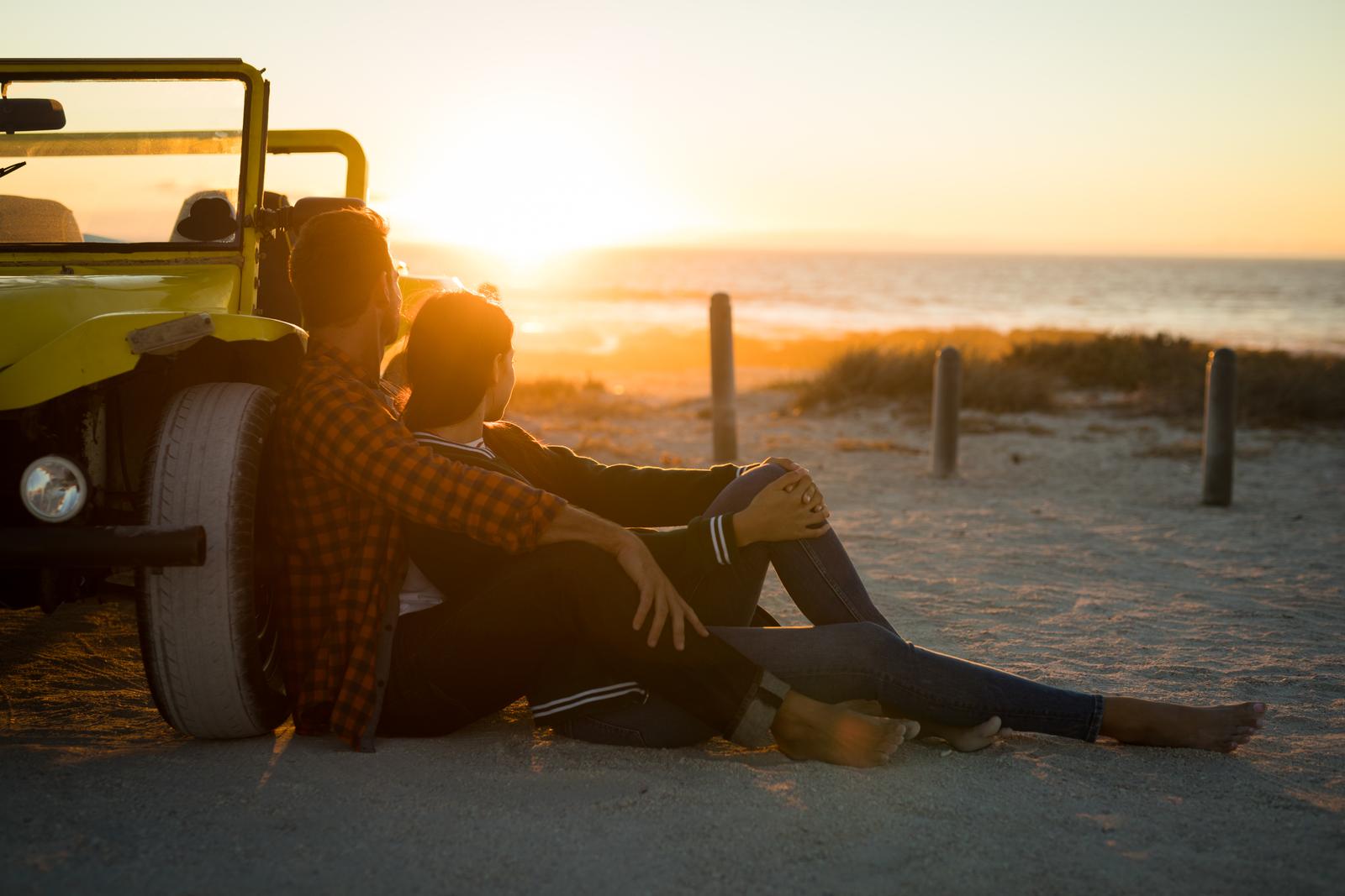 Couple sitting on beach at sunset. 