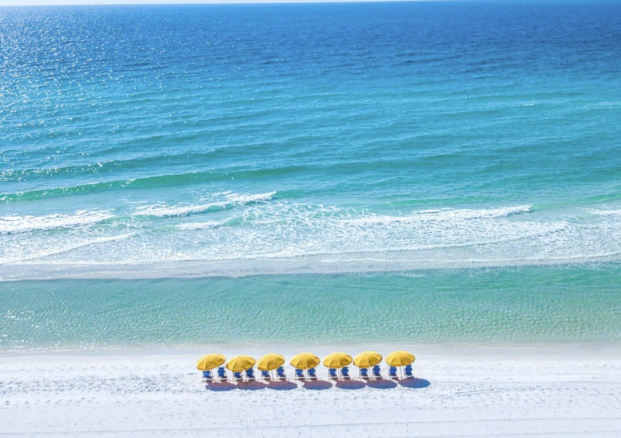 A row of yellow umbrellas on a white sand beach with crystal clear waters in Destin on the Gulf Coast of Florida. 