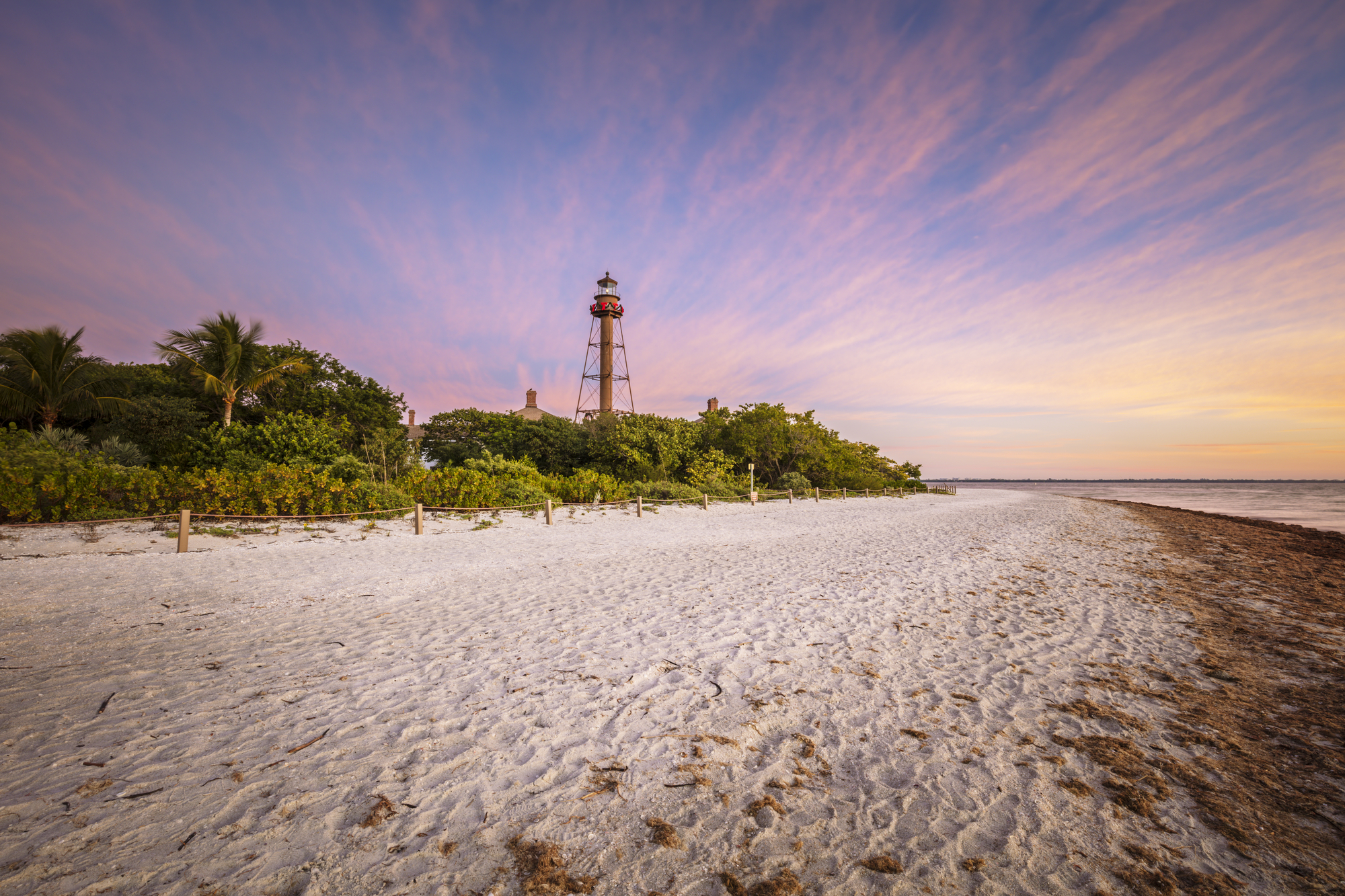 Sanibel island lighthouse at sunset with white sands and tropical greenery. 