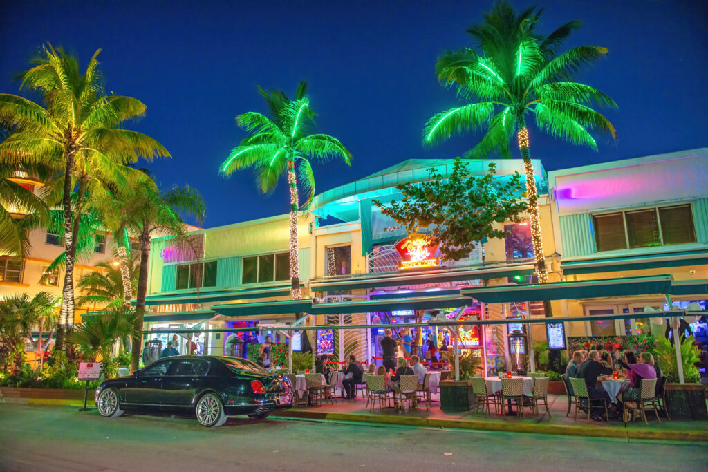 Outdoor dining in Miami at night with neon lights and palm trees.