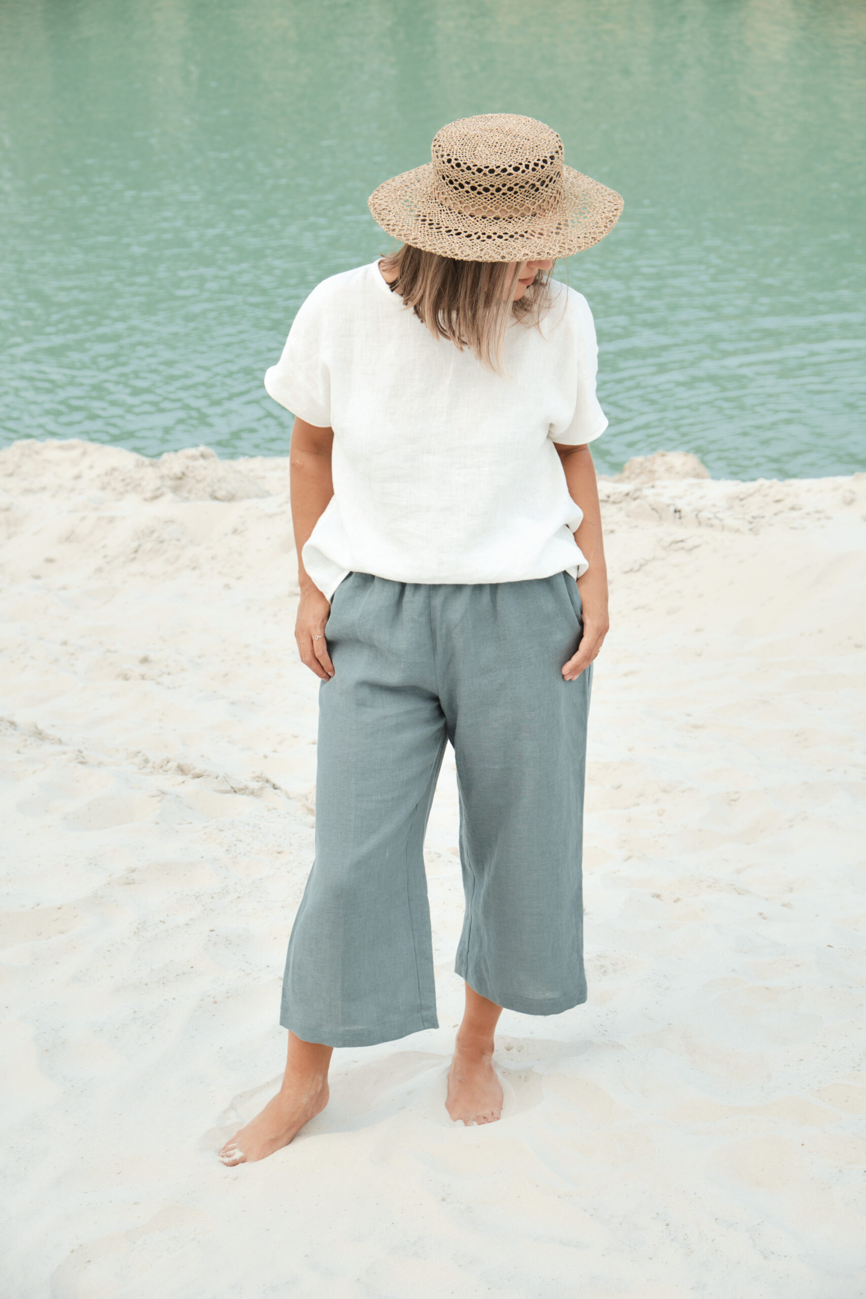 Woman standing at the beach with loose linen clothing and a hat. 