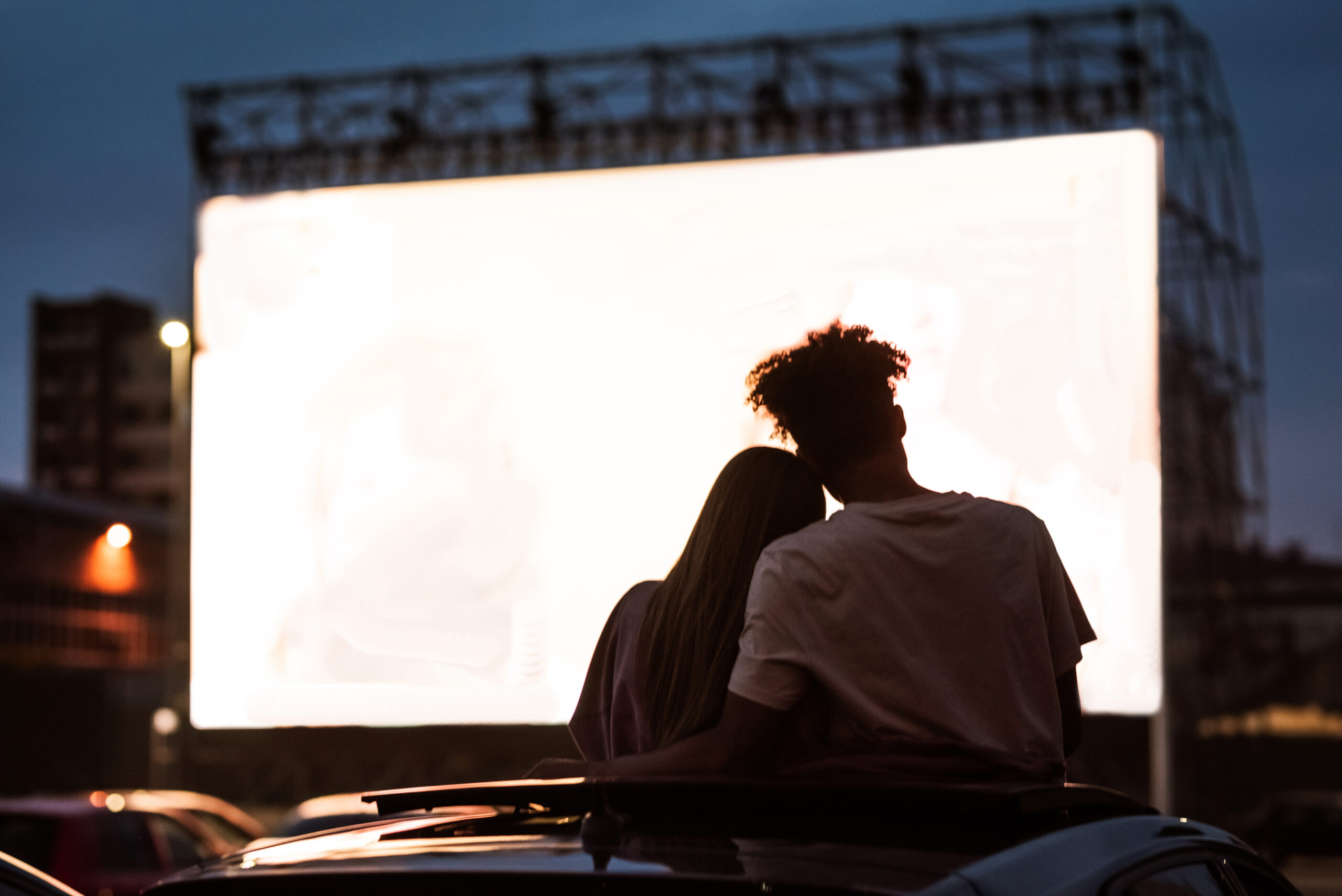 Silhouetted view of young couple watching a movie in a drive in cinema.