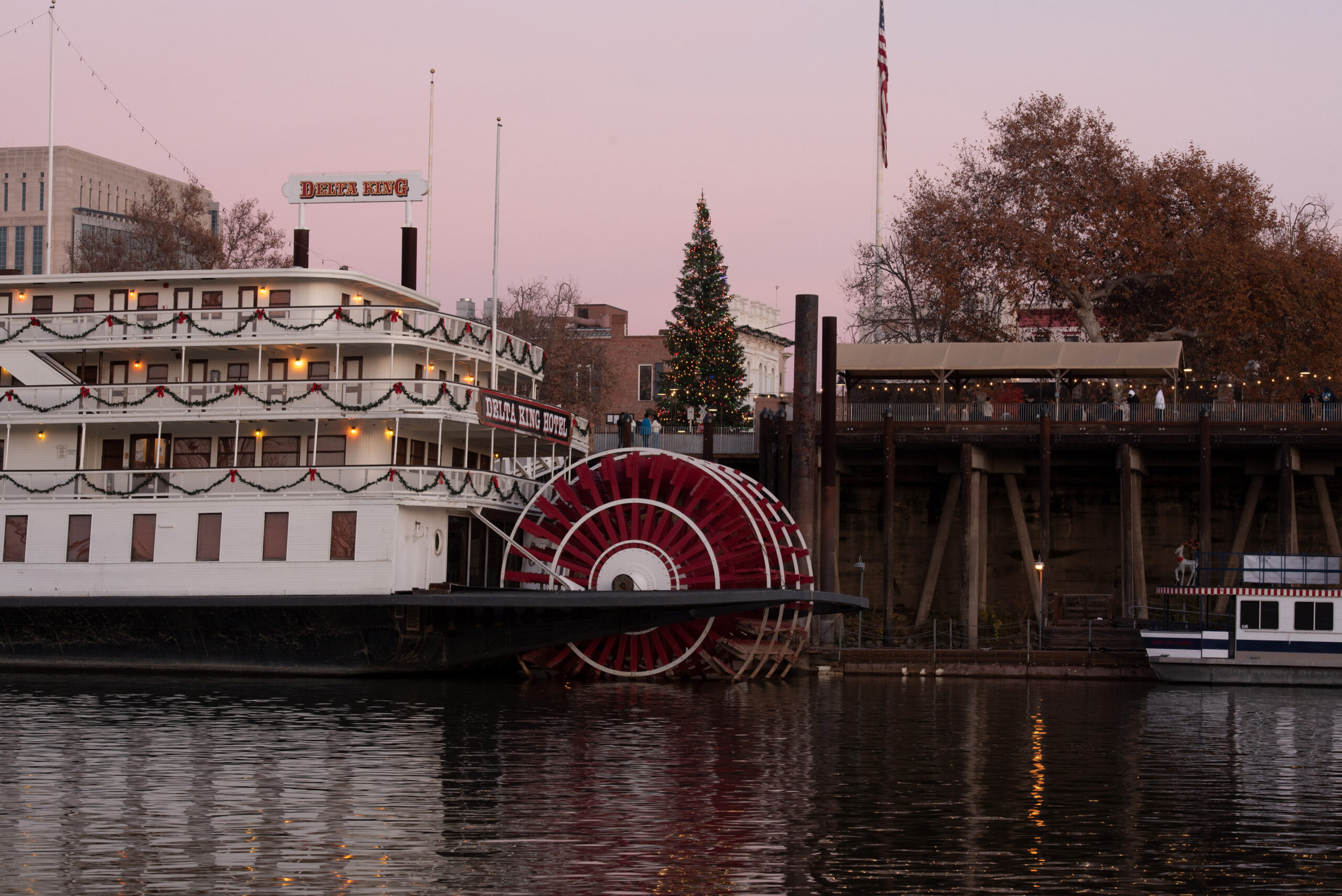 Old Sacramento with Christmas tree viewed from West Sacramento across the river, featuring part of the Delta King Hotel at sunset.