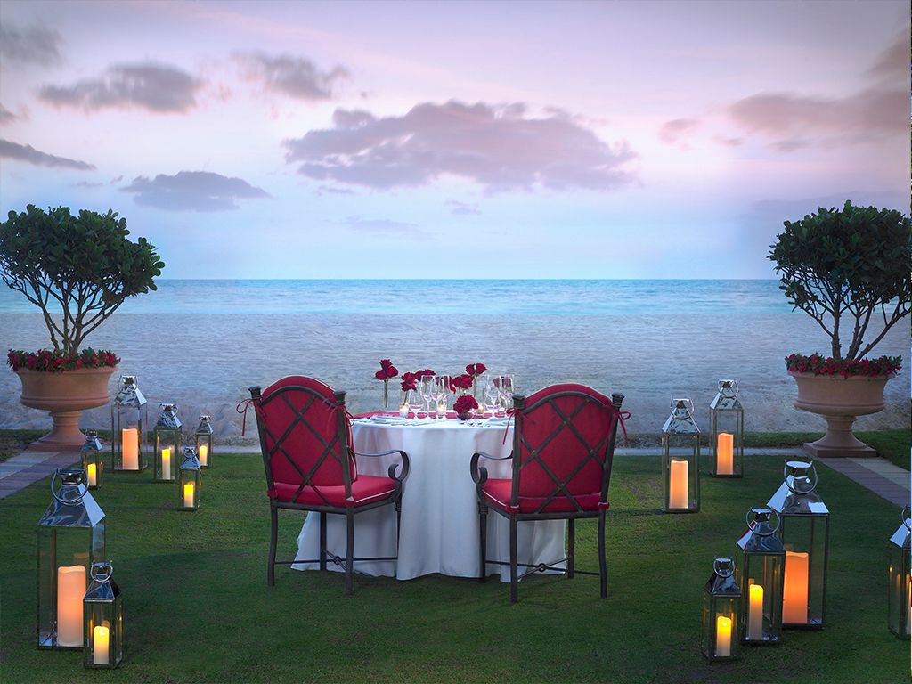 Romantic dinner by the water with candles and roses at dusk.