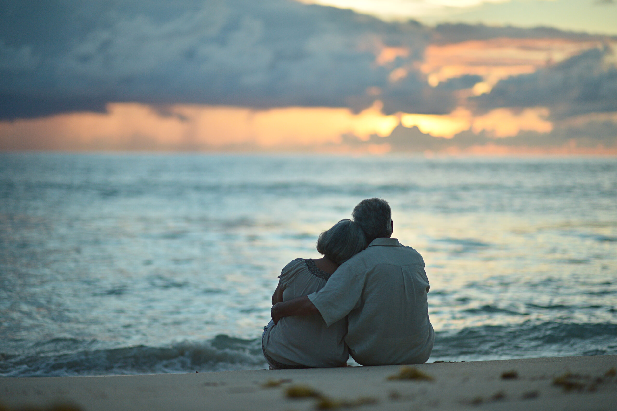 Elderly couple sitting at the beach at sunset.