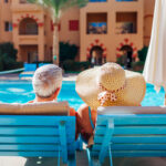 Senior couple relaxing by swimming pool lying on chaise-longues. People enjoying vacation.
