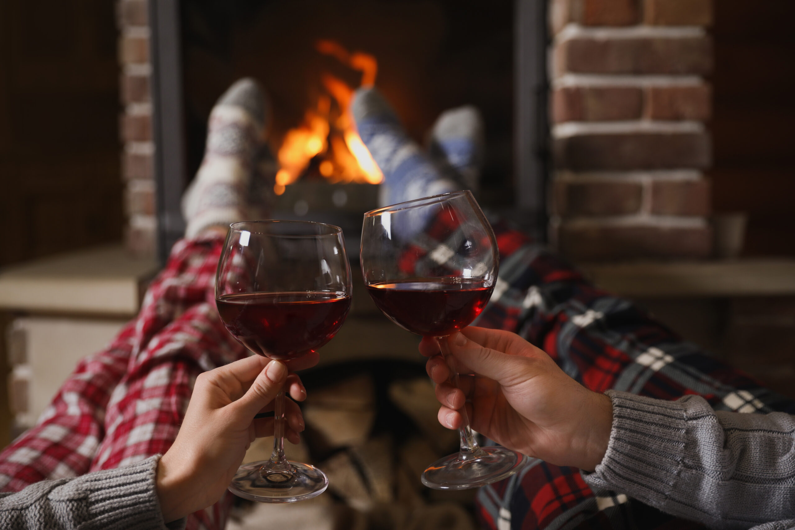 Couple with glasses of red wine near burning fireplace.