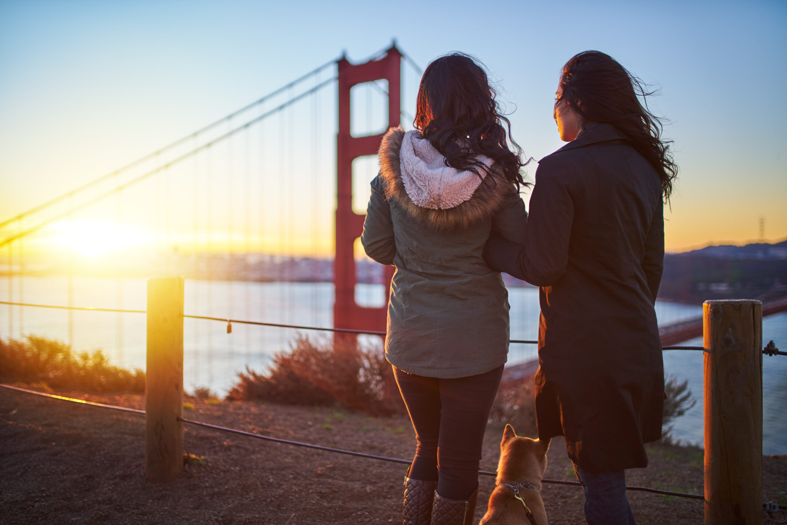 Young female couple with dog at golden gate bridge viewing the sunset in San Francisco.