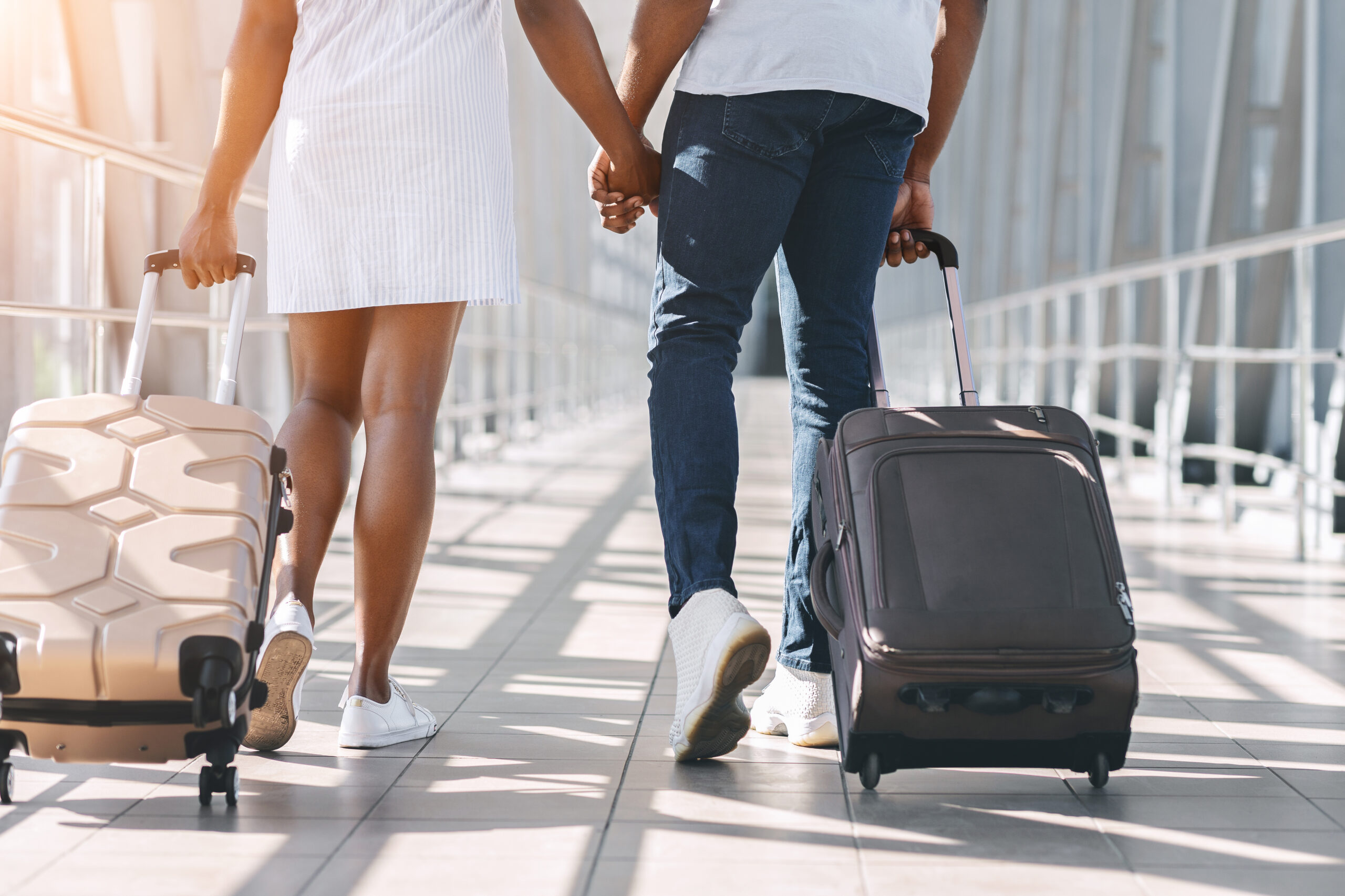 Black millennial couple walking with luggage at airport building.