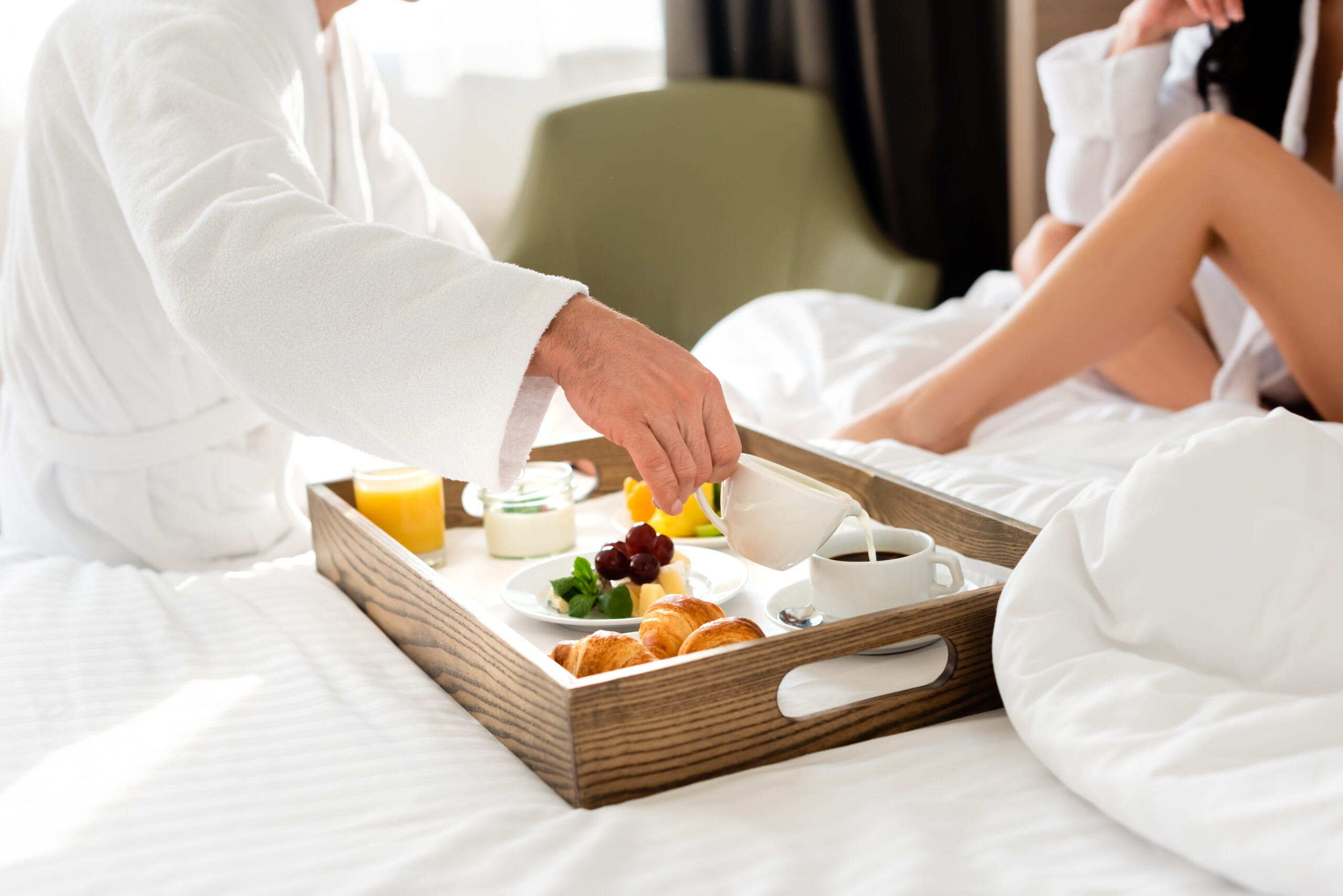 A man pouring cream into a mug of coffee, enjoying breakfast in bed with his partner.