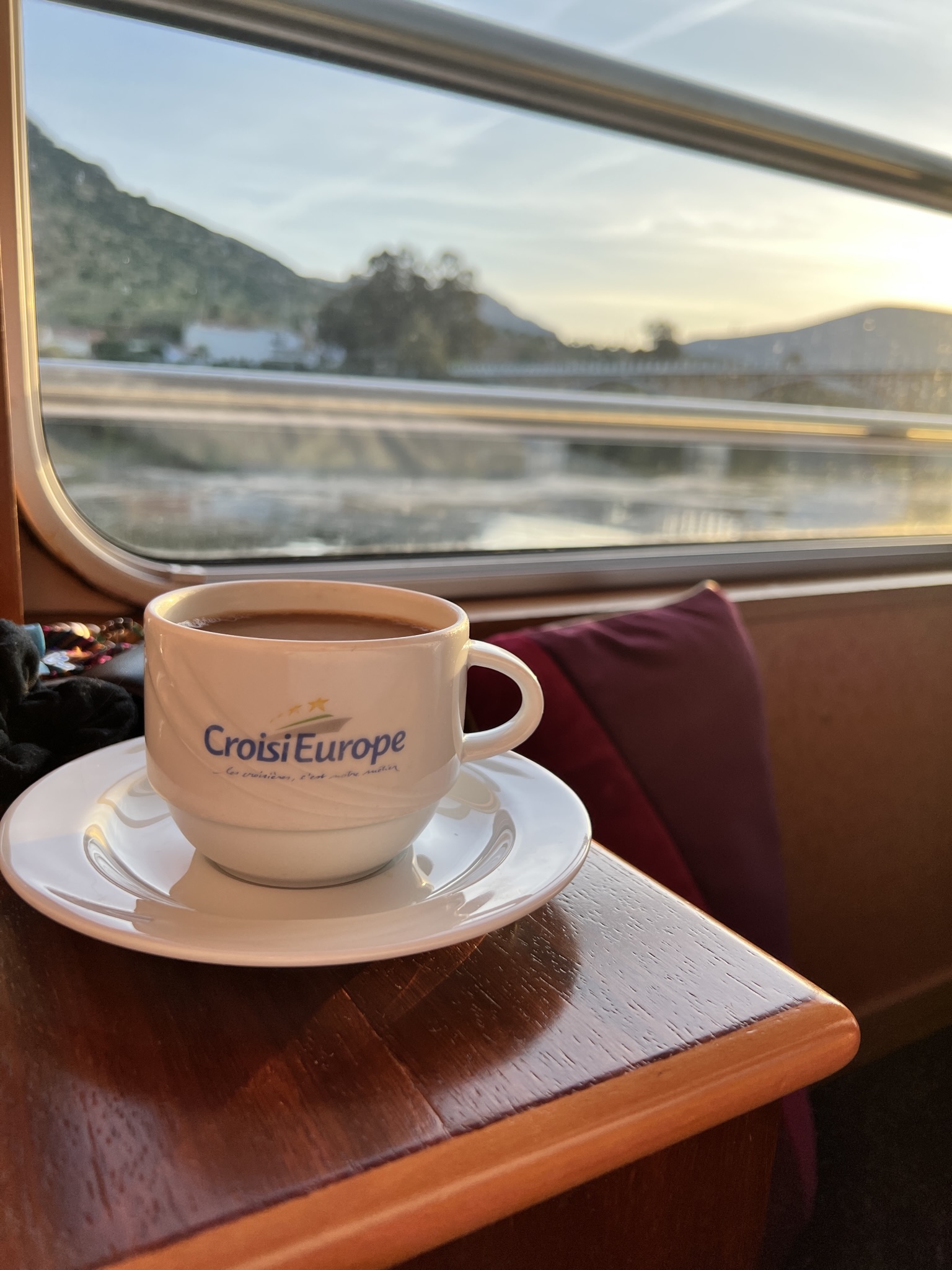Cup of coffee in front of cabin view on river cruise.