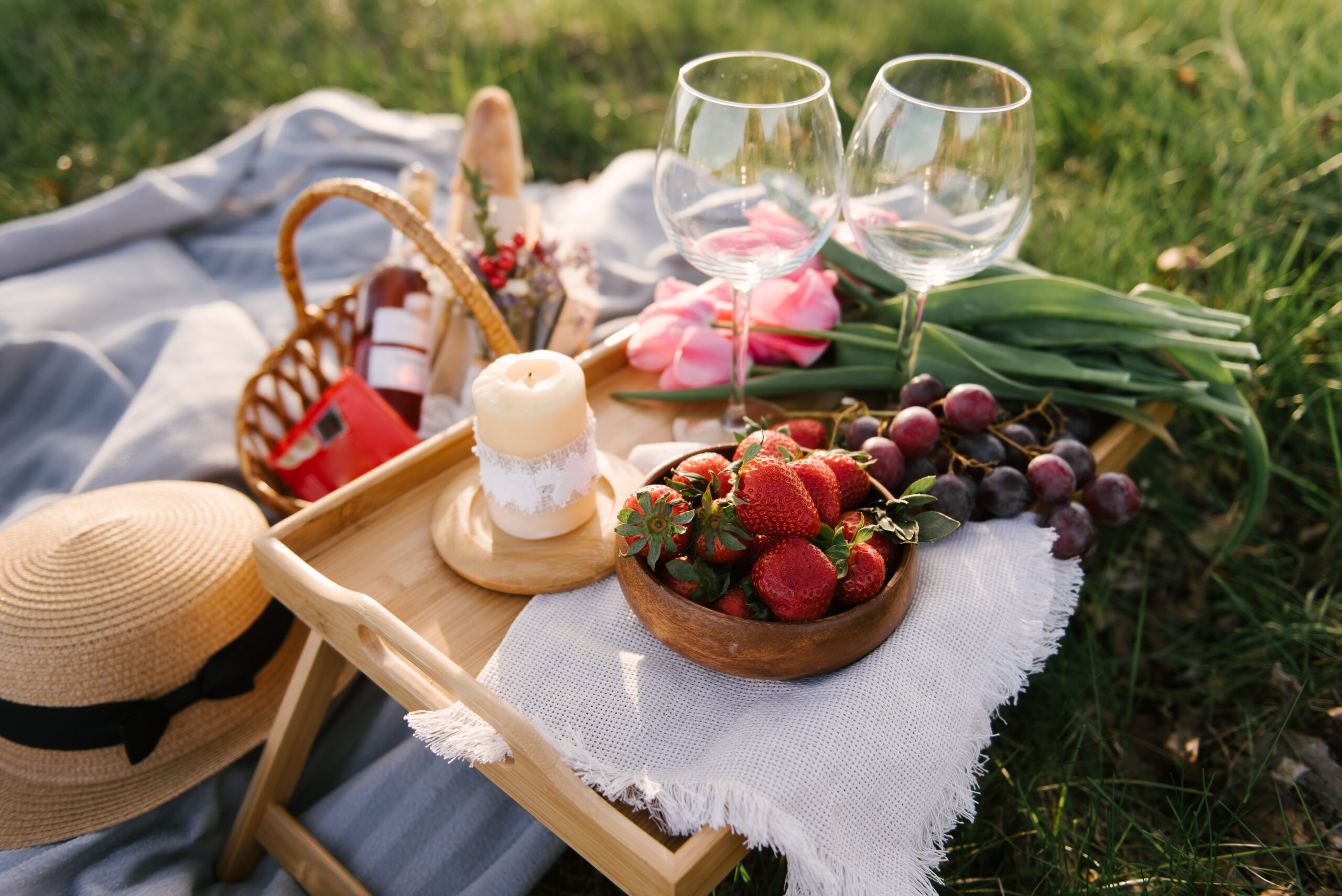 Picnic basket with strawberries, grapes and buns on the green grass in the garden