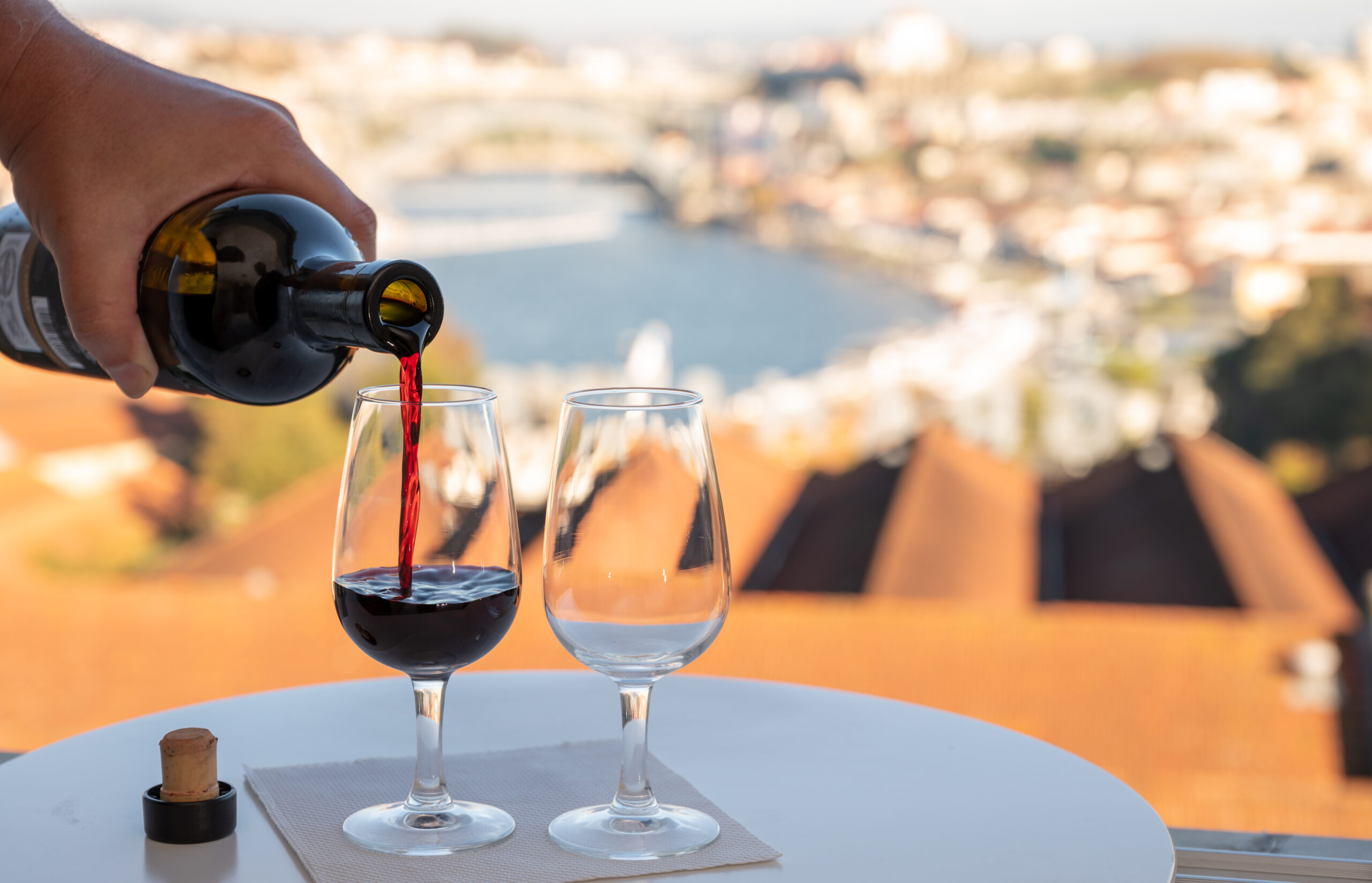 Pouring of fortified dessert ruby, tawny port wines in glasses with view on Douro river, porto lodges of Vila Nova de Gaia and city of Porto, Portugal, on sunset