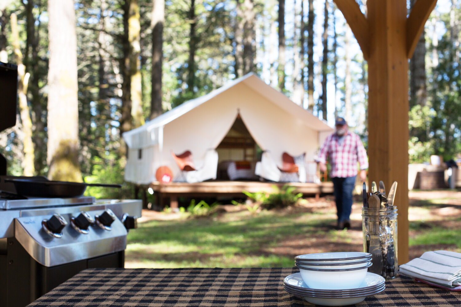 Glamping tent in the woods behind a outdoor grill and picnic table, a secluded romantic getaways in the USA.