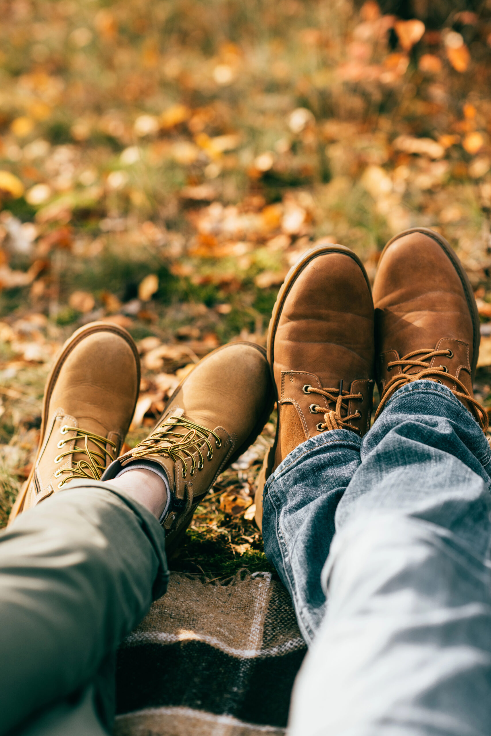 Shot of a couples brown boots and jeans over a picnic blanket surrounded by fall leaves.