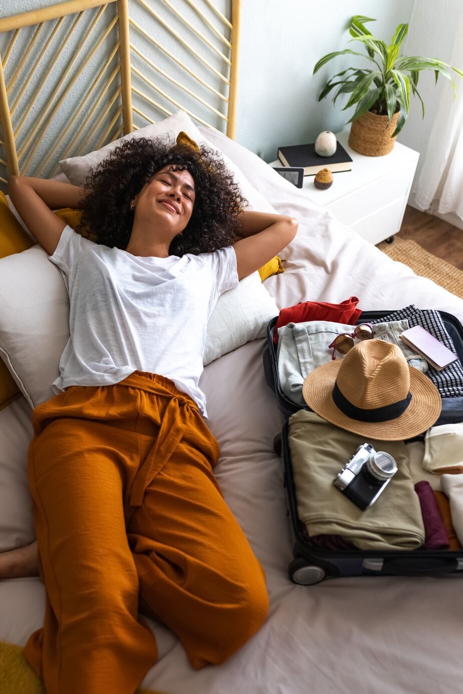Woman lying down on bed next to open suitcase full of clothes.