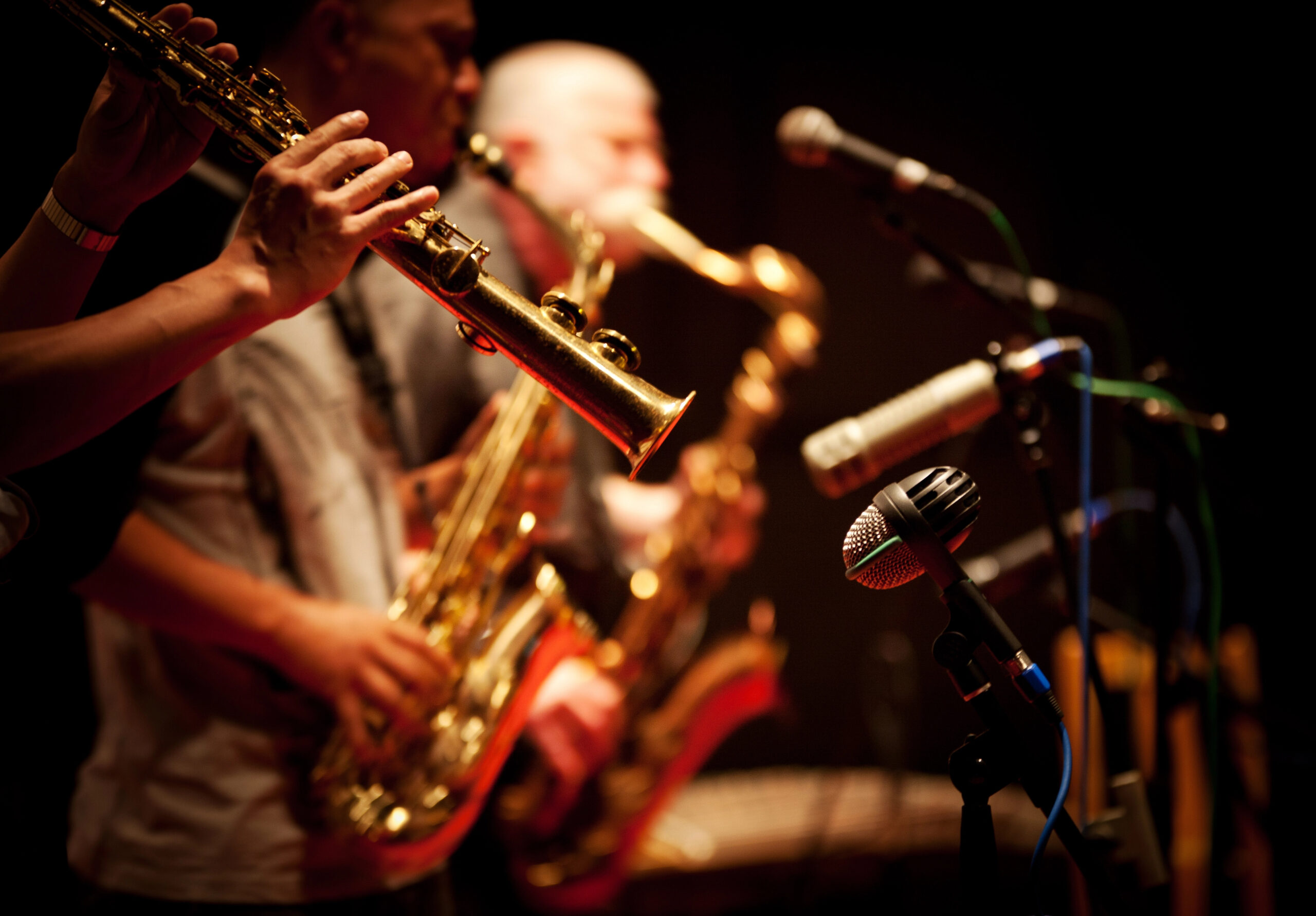Side view of jazz musicians playing saxophone under a spotlight.