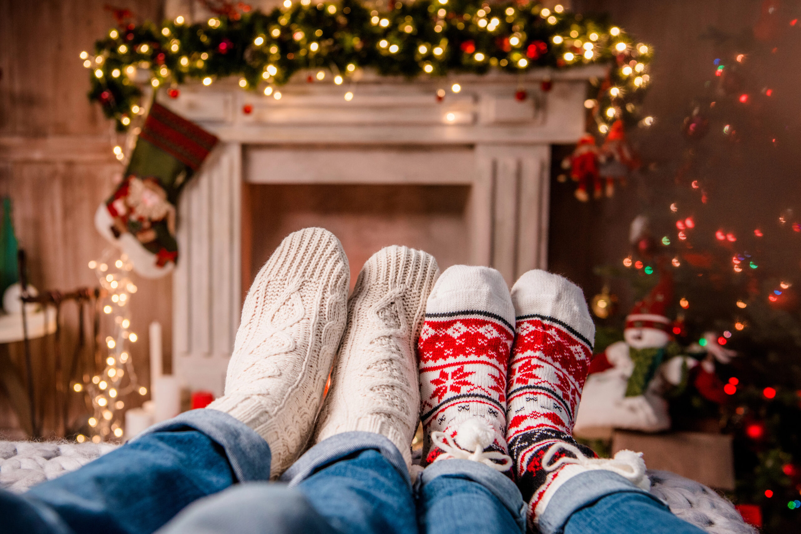 Festive sock-clad feet rest by a decorated fireplace near a Christmas tree.