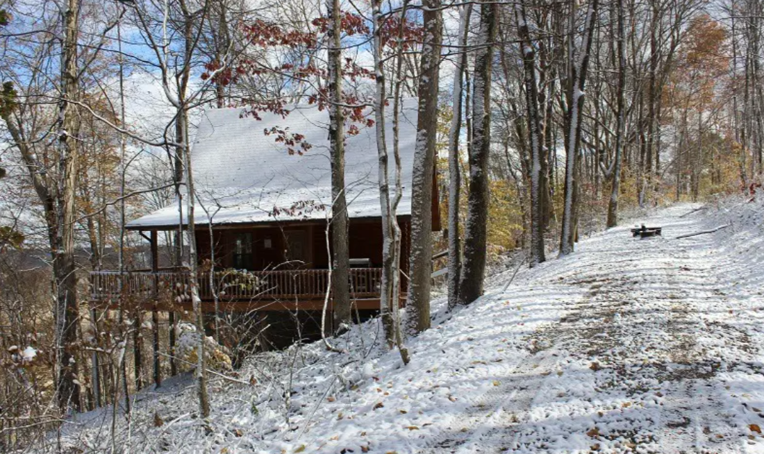 A wooden cabin sits amidst trees on a snowy hillside with a path leading up to it. It's one of the most romantic getaways in December.