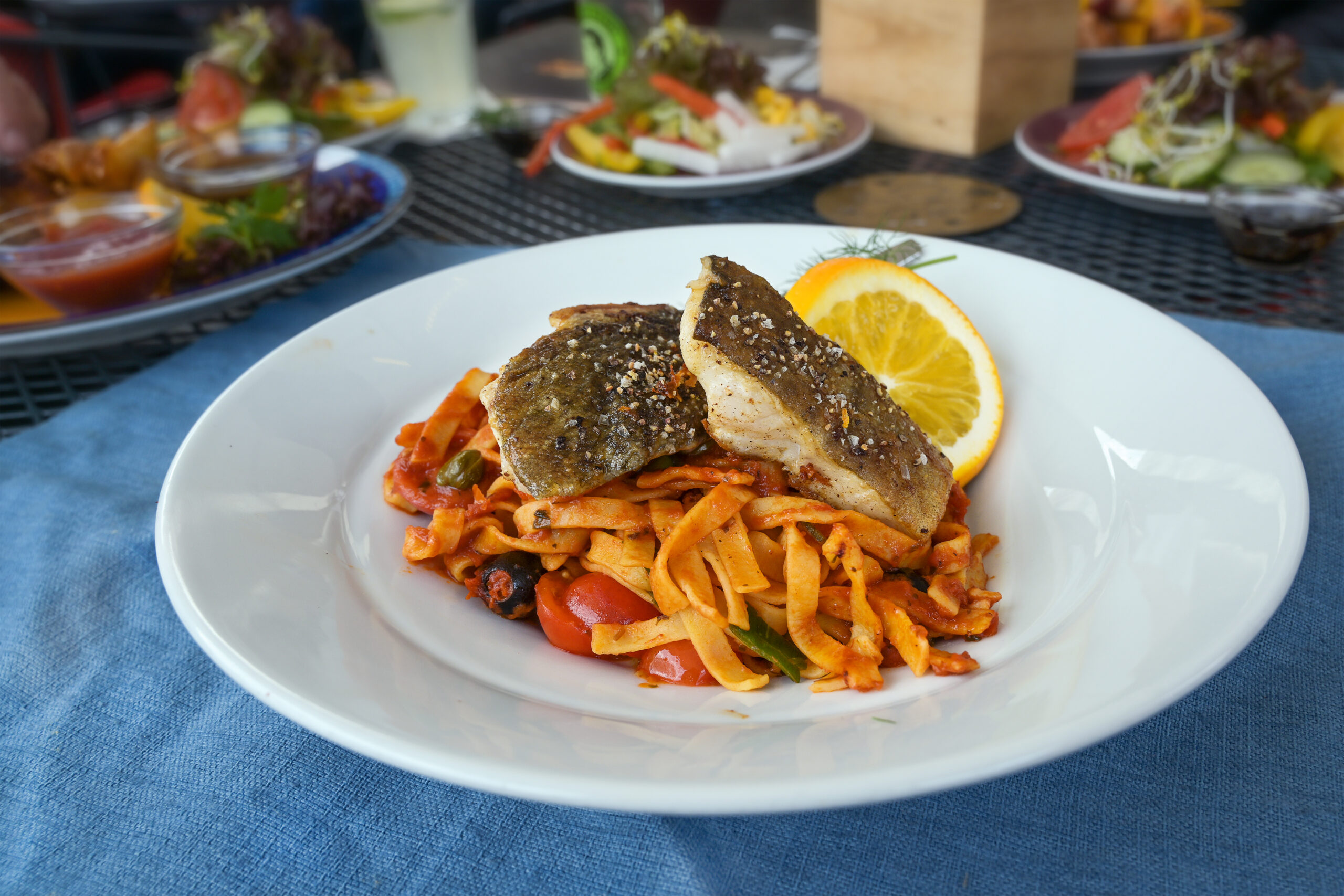Lemon Roasted codfish with Cajun pasta serve on a  white plate and blue napkin on a table at a dinner.