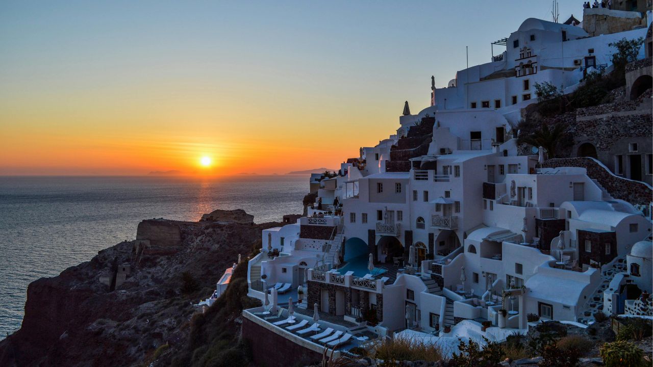 Sunset over whitewashed cliffside buildings in Oia, Santorini, Greece.
