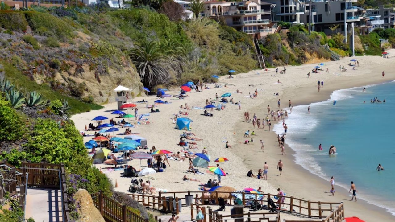 Crowded sandy beach with colorful umbrellas, beachgoers, and oceanfront houses on a sunny day.
