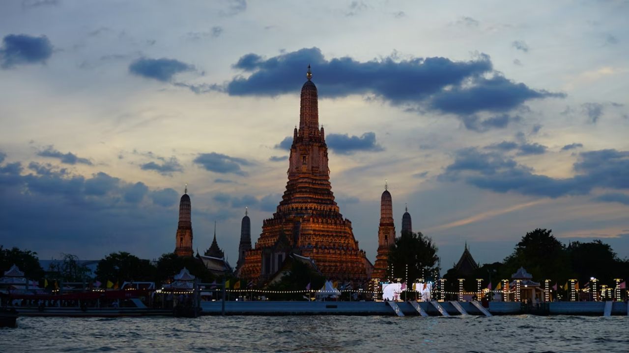 Wat Arun temple glowing at dusk by the Chao Phraya River, Bangkok, Thailand.