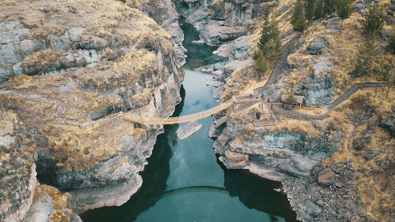 Aerial view of a narrow rope bridge spanning a deep rocky canyon over a river
