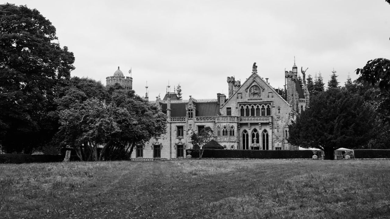 Black and white photo of an abandoned Gothic-style castle surrounded by trees.