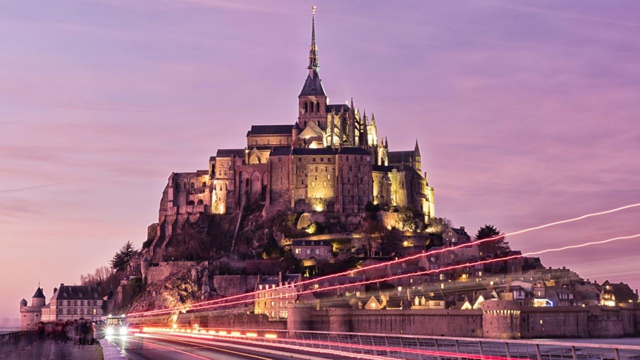Mont Saint-Michel illuminated at dusk with light trails on the causeway in Normandy, France.