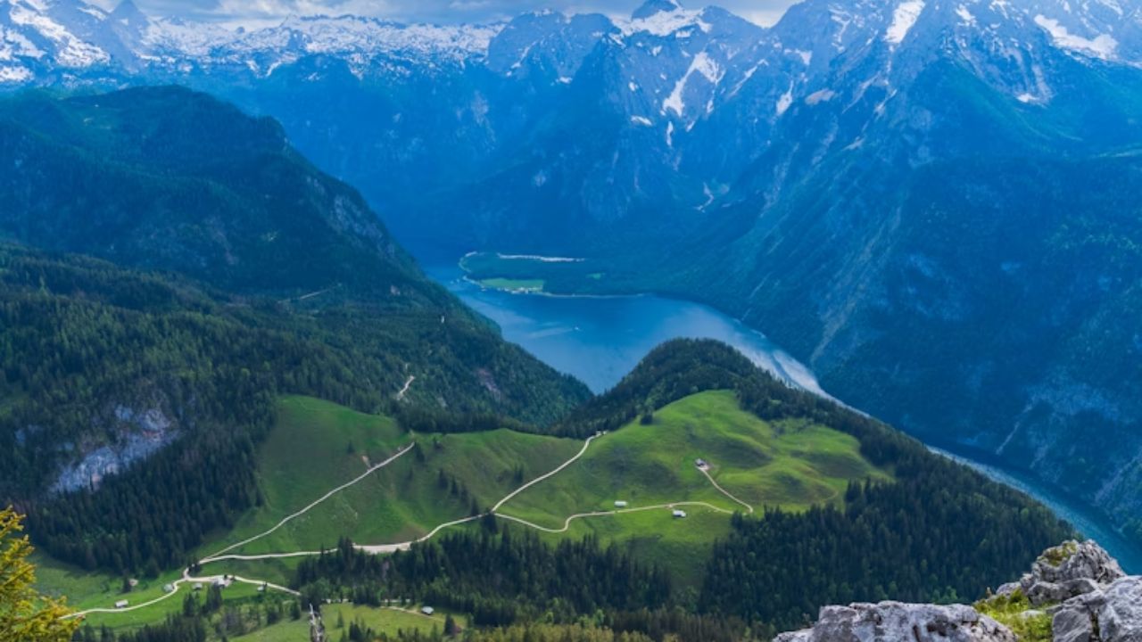 Aerial view of Königssee Lake in Bavaria, Germany, surrounded by alpine peaks and green meadows.