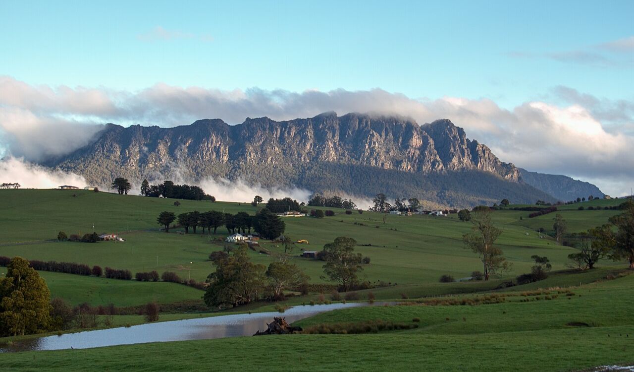 Jagged mountain ridge towers above lush green fields in Tasmania
