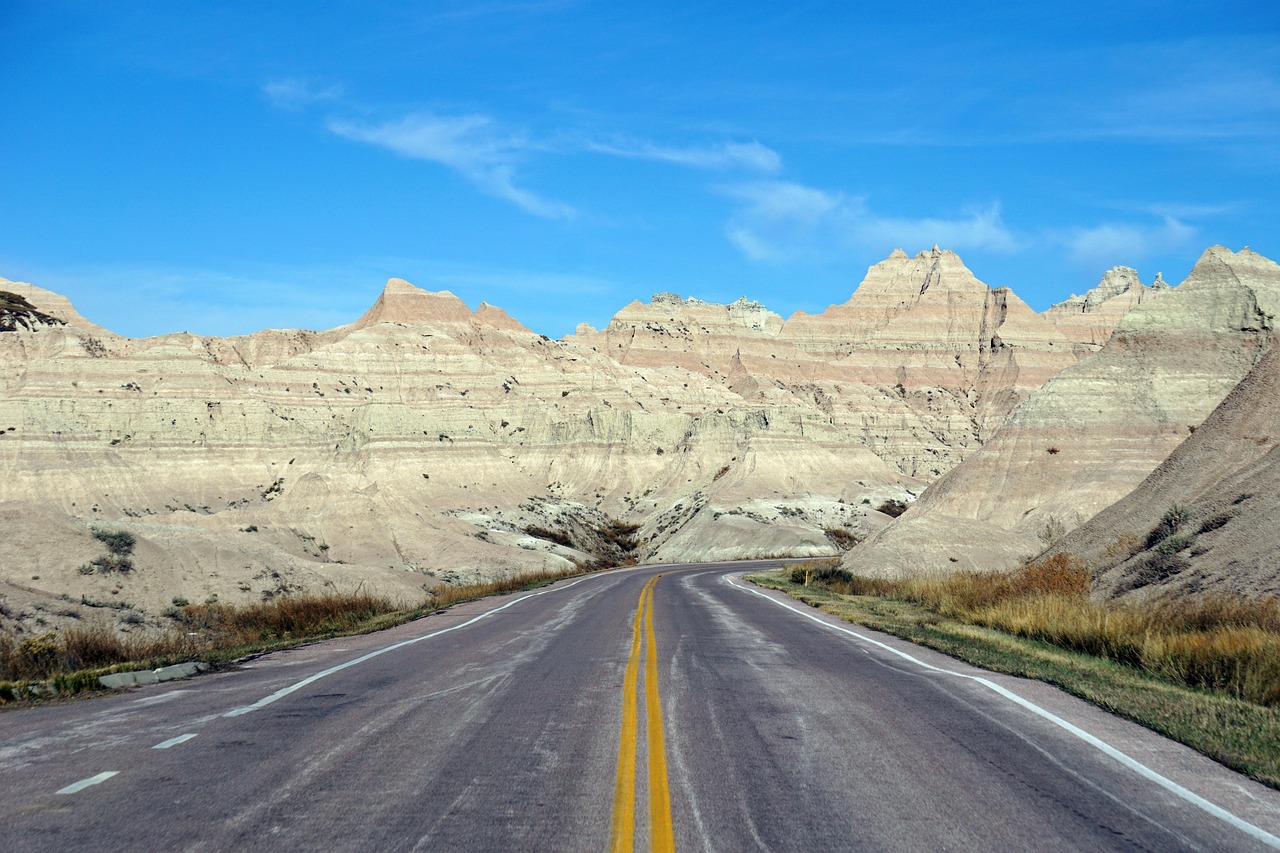 A paved road with yellow lines curves through a rocky desert under a clear blue sky.
