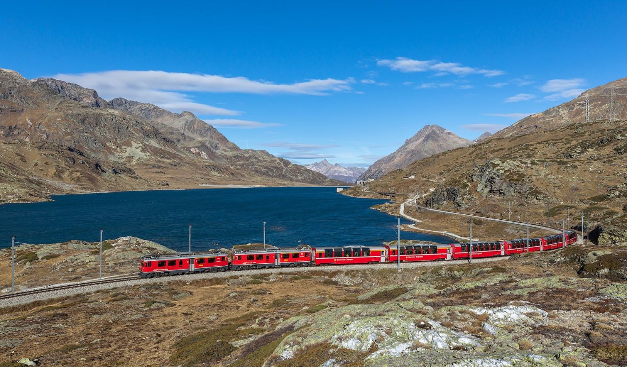 The red Bernina Express train curves through the Swiss Alps beside a deep blue lake