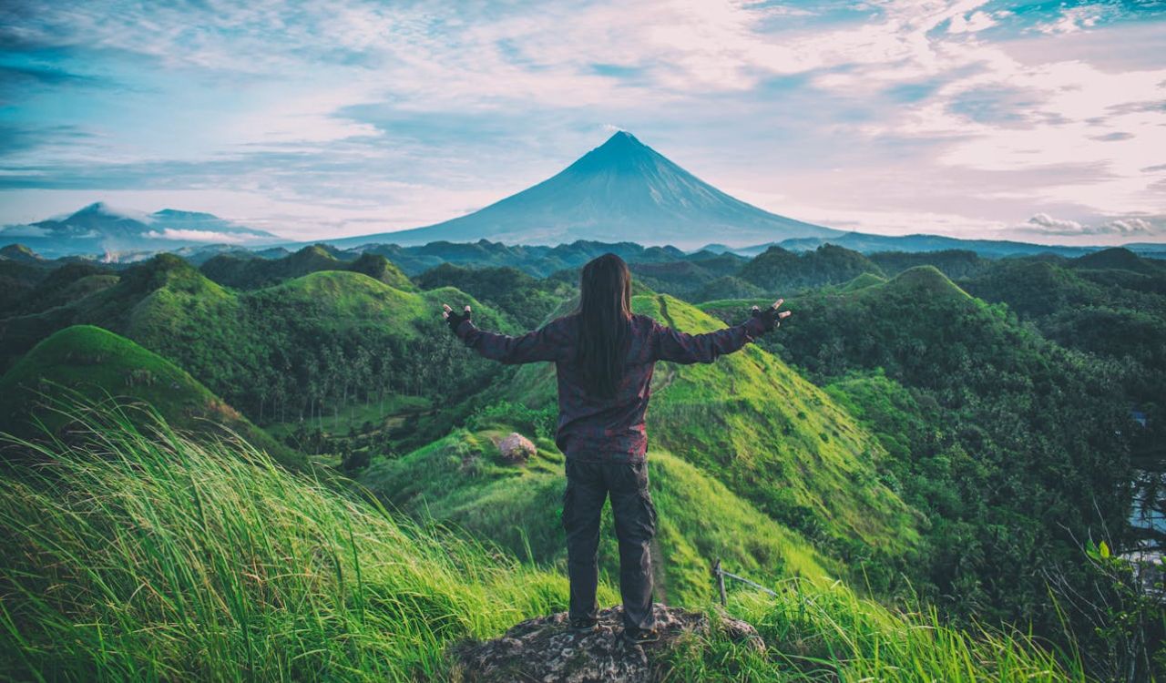 Solo traveler embraces the view of a distant volcano from a green hilltop