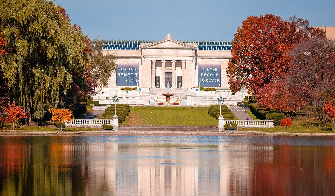 Front view of the Cleveland Museum of Art with fall trees reflected in a calm lake