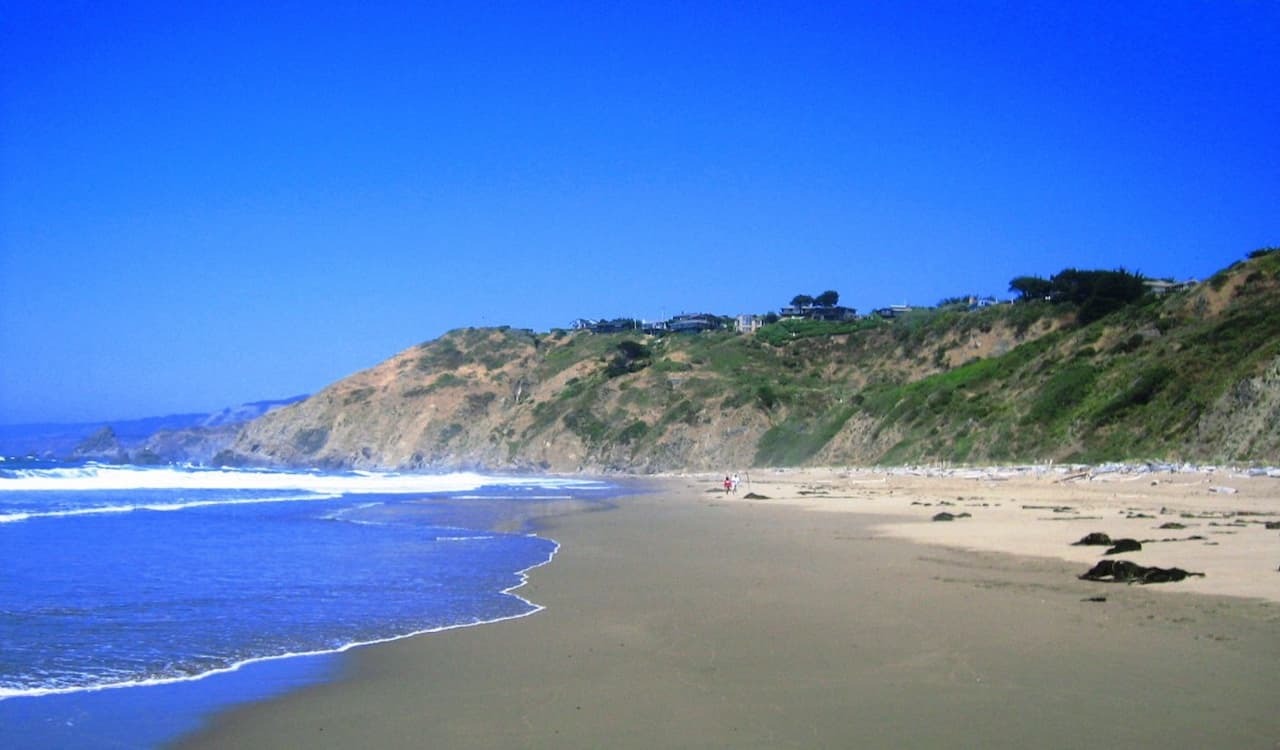Wide sandy beach with cliffs under clear blue sky in Elk, California.