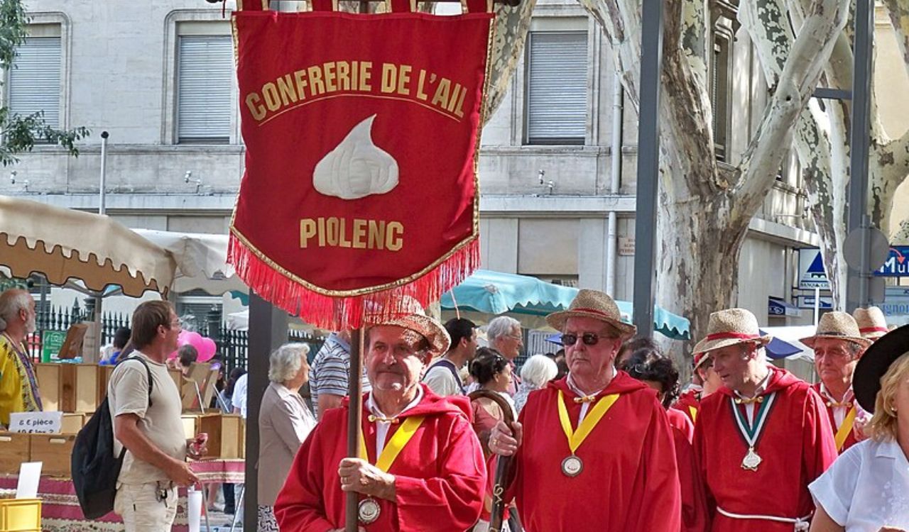 People in red robes and straw hats parade with a garlic-themed banner at the Festival de l’ail in France