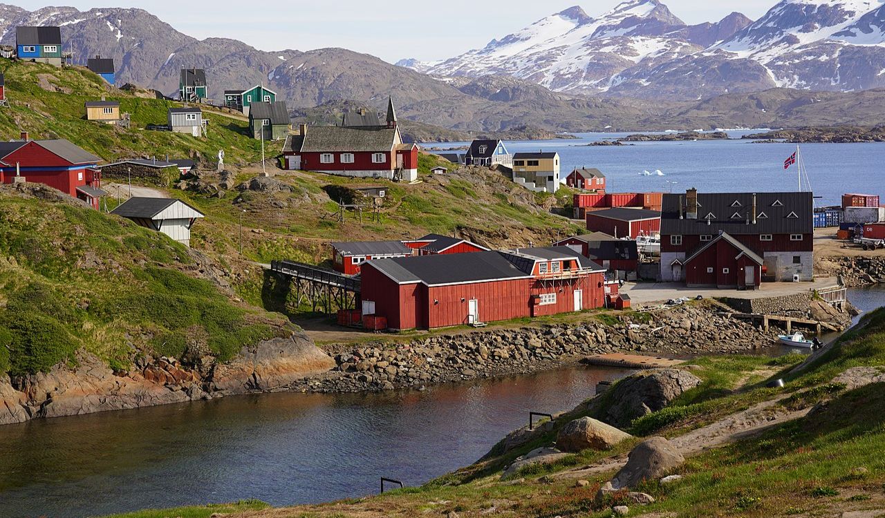 Colorful houses line Greenland’s rugged coast, with icy mountains reflecting in clear Arctic waters