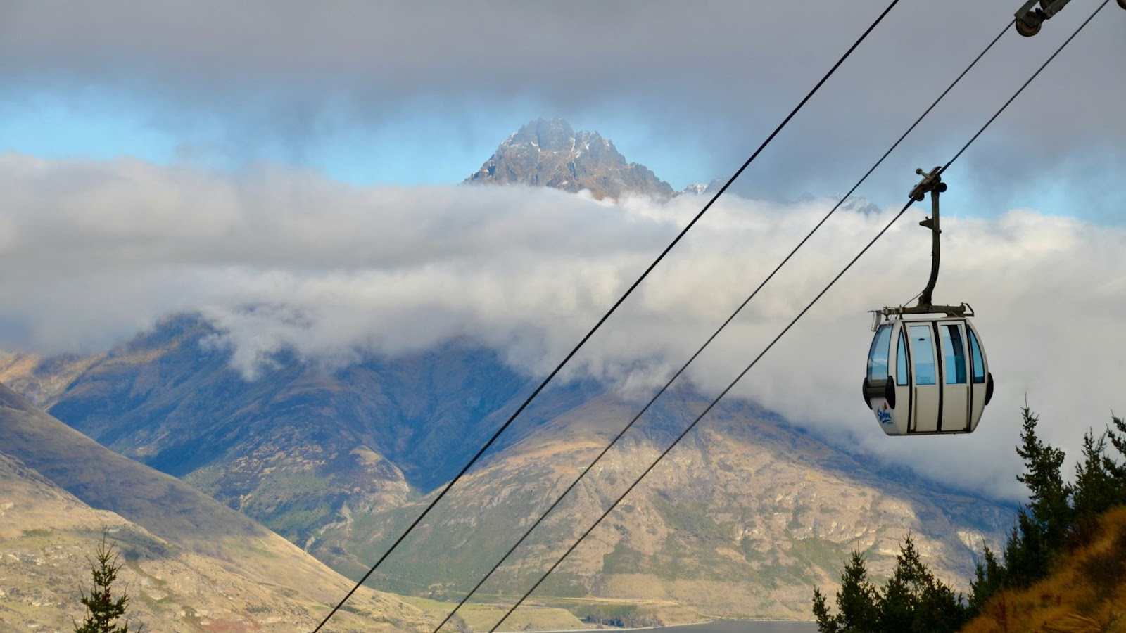 A cable car moves along a wire above mountains partly obscured by clouds.
