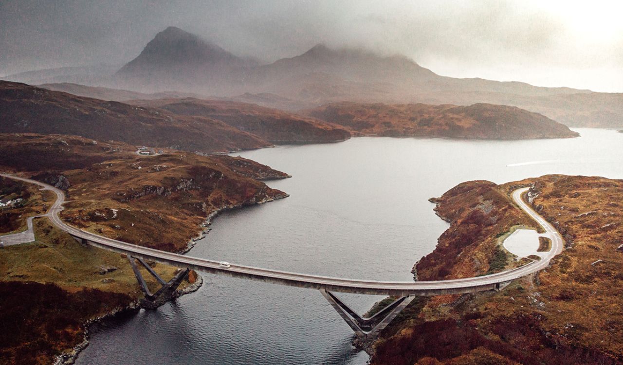 Curving bridge on Scotland’s North Coast 500 route with misty mountains in the background