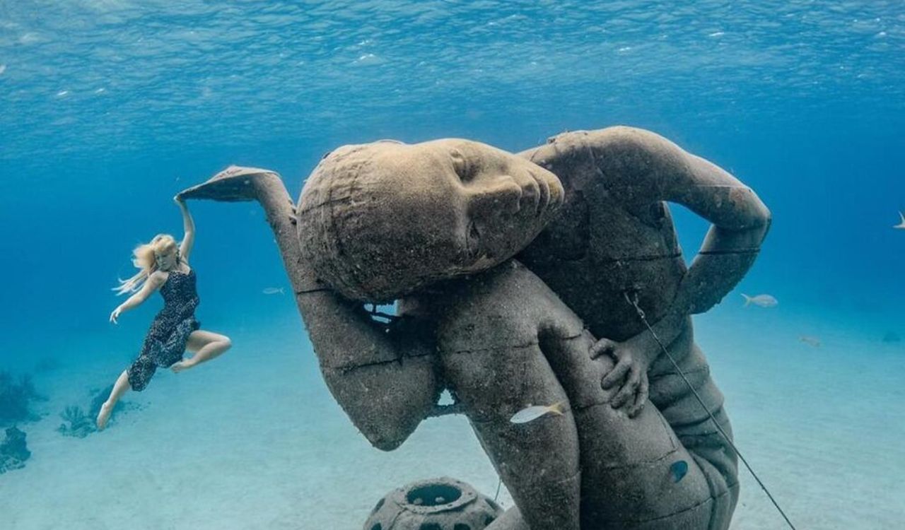 Underwater sculpture of Ocean Atlas in the Bahamas with a diver swimming nearby
