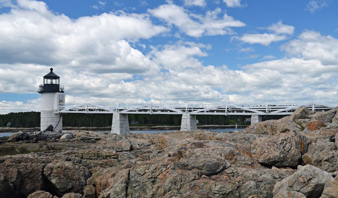 White lighthouse and footbridge on rocky shore in Port Clyde, Maine.