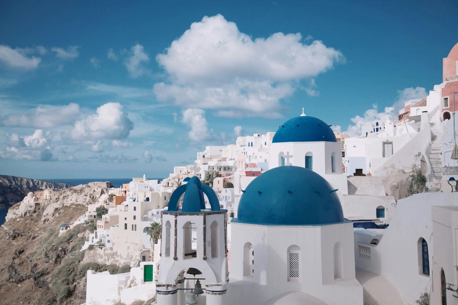 White buildings with blue domes overlook the sea from a hillside under a partly cloudy sky in Santorini, Greece.