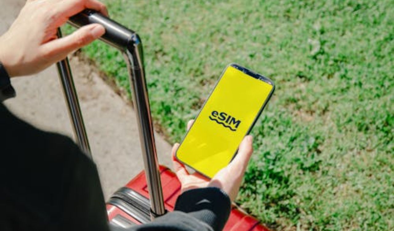 Traveler holding phone displaying eSIM next to red suitcase
