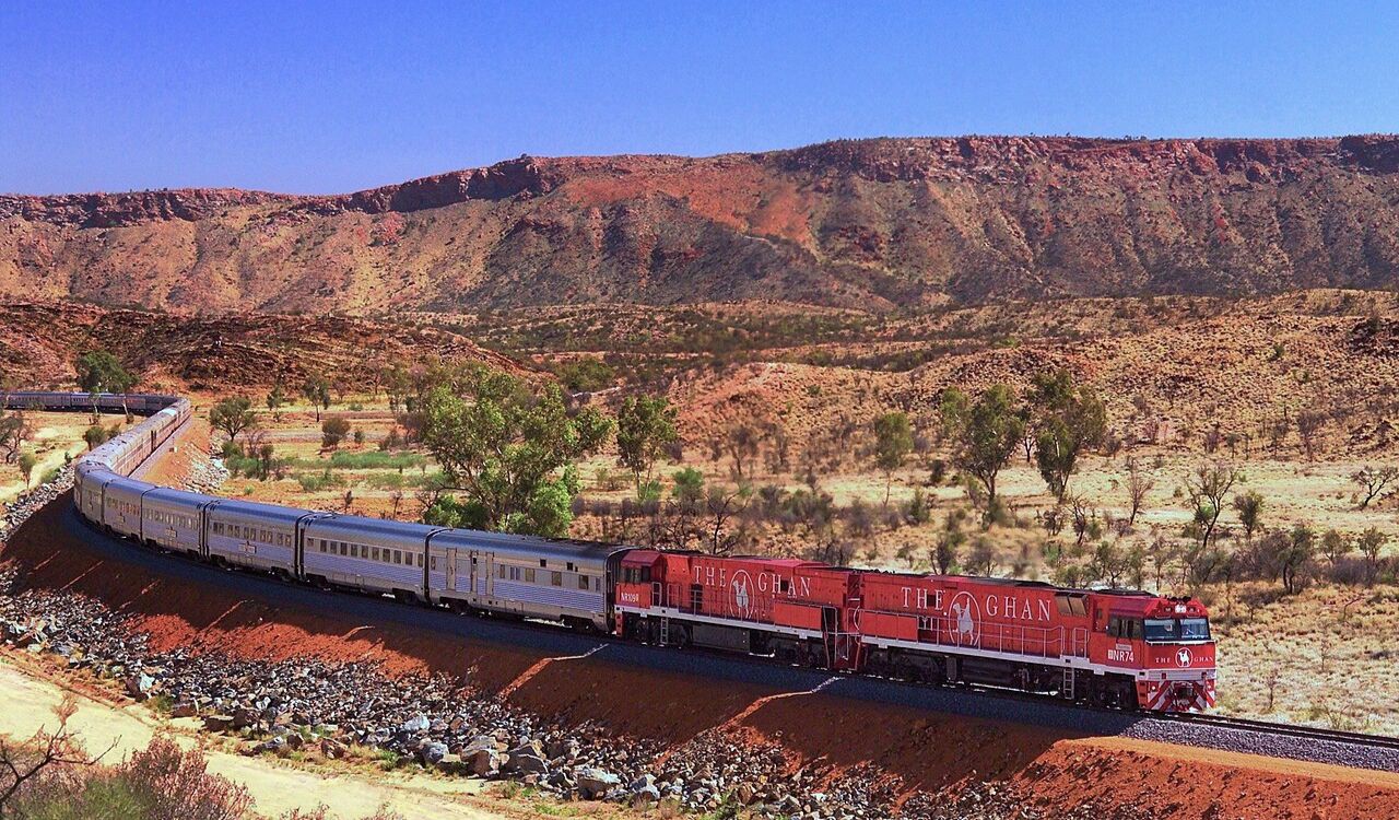The Ghan train winds through Australia's red desert landscape under a clear blue sky