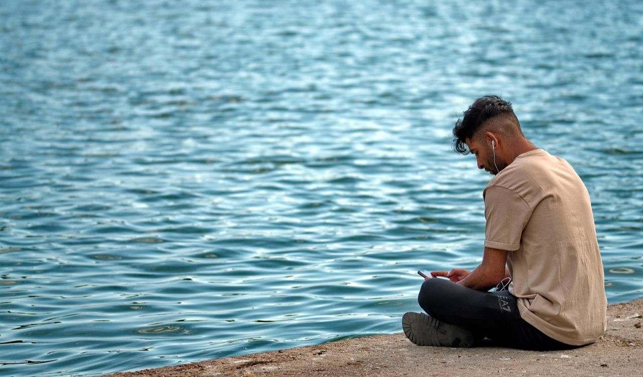 Solo traveler sitting by the water, calmly listening to music, trusting his instincts in a quiet moment