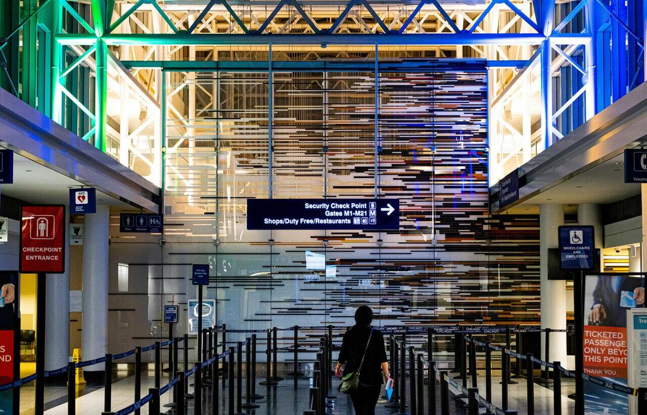 Traveler walking toward security checkpoint under colorful lights at airport.