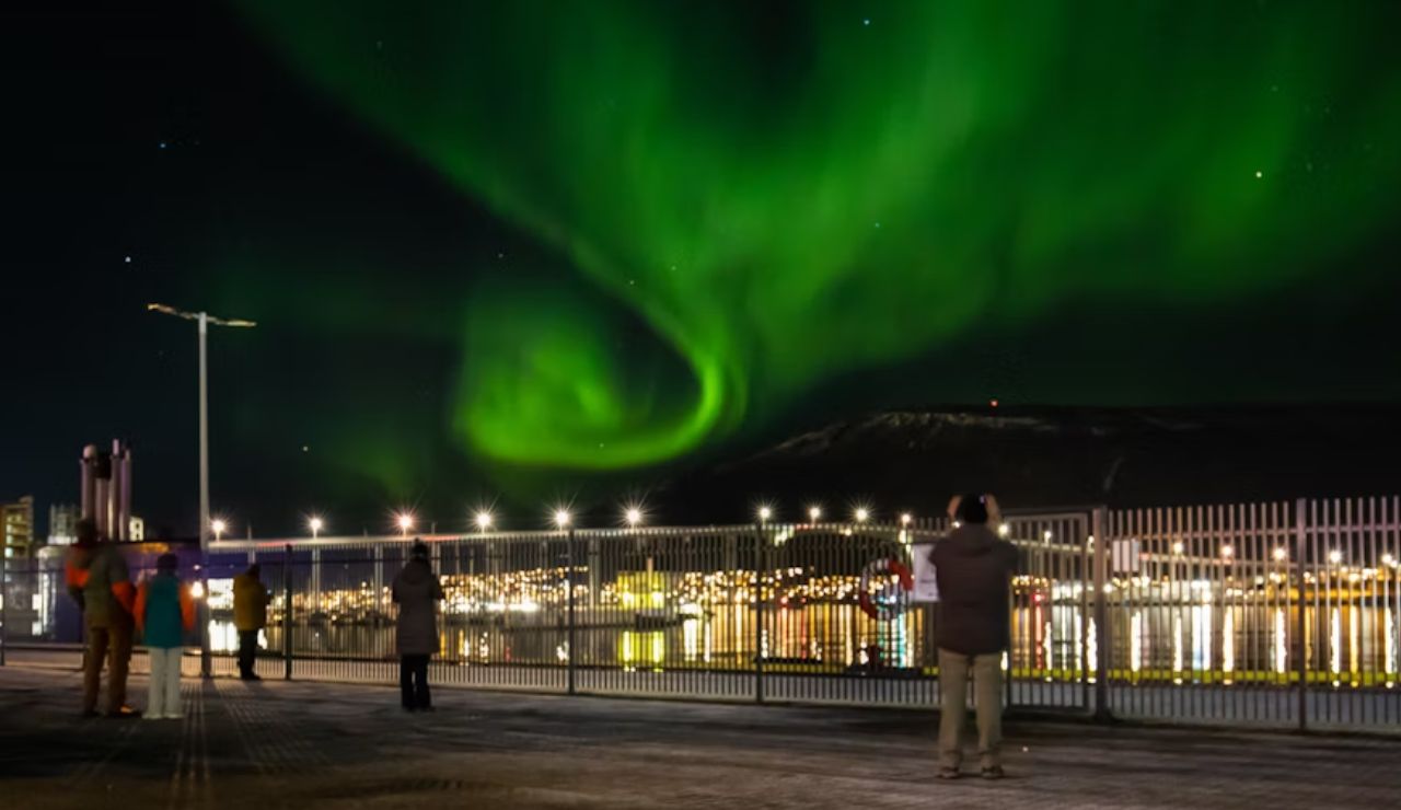People watching the northern lights swirl over the waterfront in Alta, Norway.